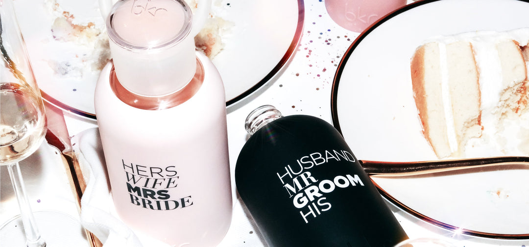 Wedding scene with a pink bkr glass water bottle with Bride printed sleeve and a black bkr glass bottle with a Groom print