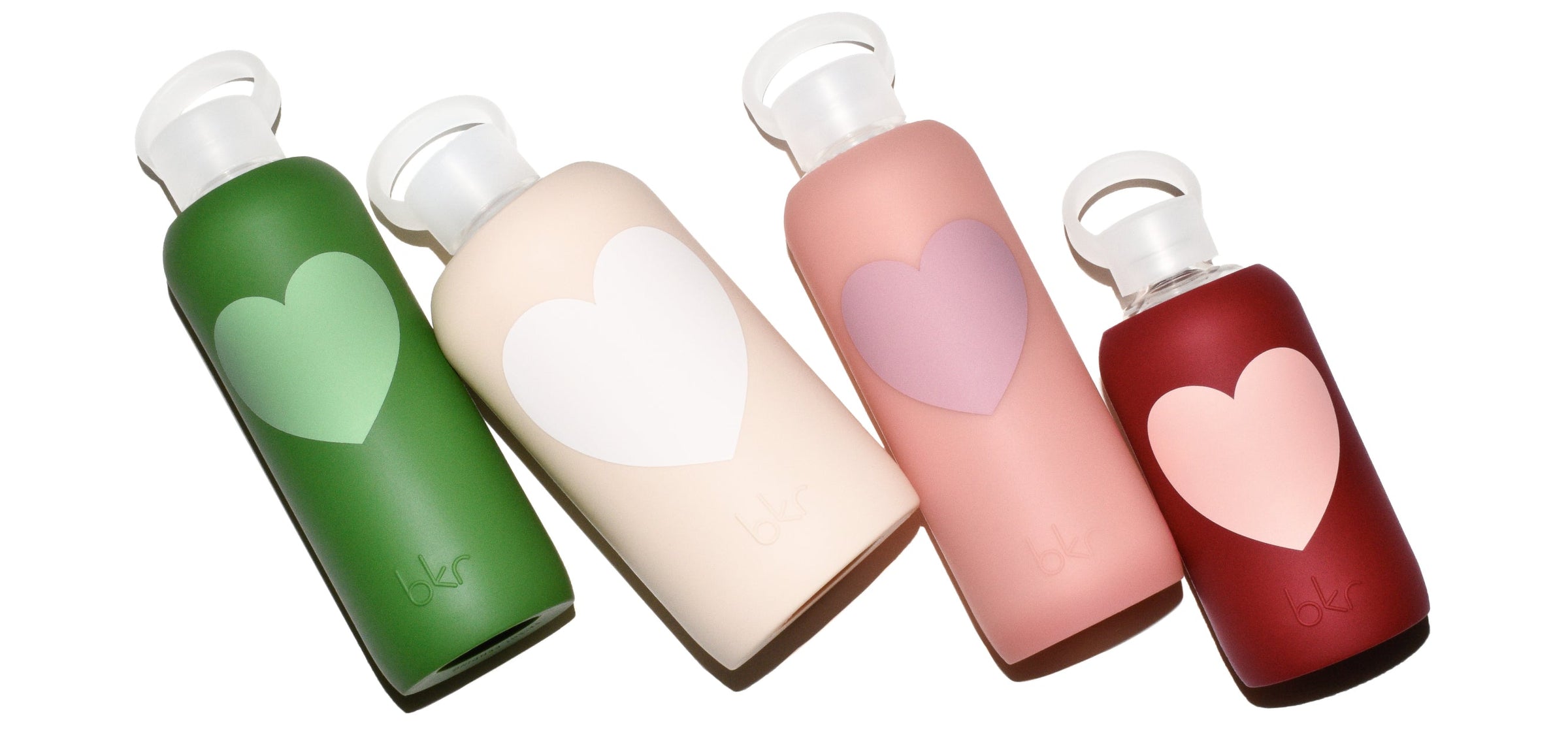 Reusable glass and silicone water bottles in opaque fern with matcha green heart, opaque linen with seashell white heart, sheer blushed beige coral with dusty rose heart, and opaque Venice brick red with light Paris-ish peach heart.