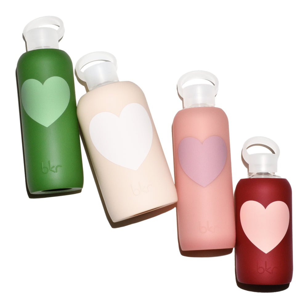 Reusable glass and silicone water bottles in opaque fern with matcha green heart, opaque linen with seashell white heart, sheer blushed beige coral with dusty rose heart, and opaque Venice brick red with light Paris-ish peach heart.