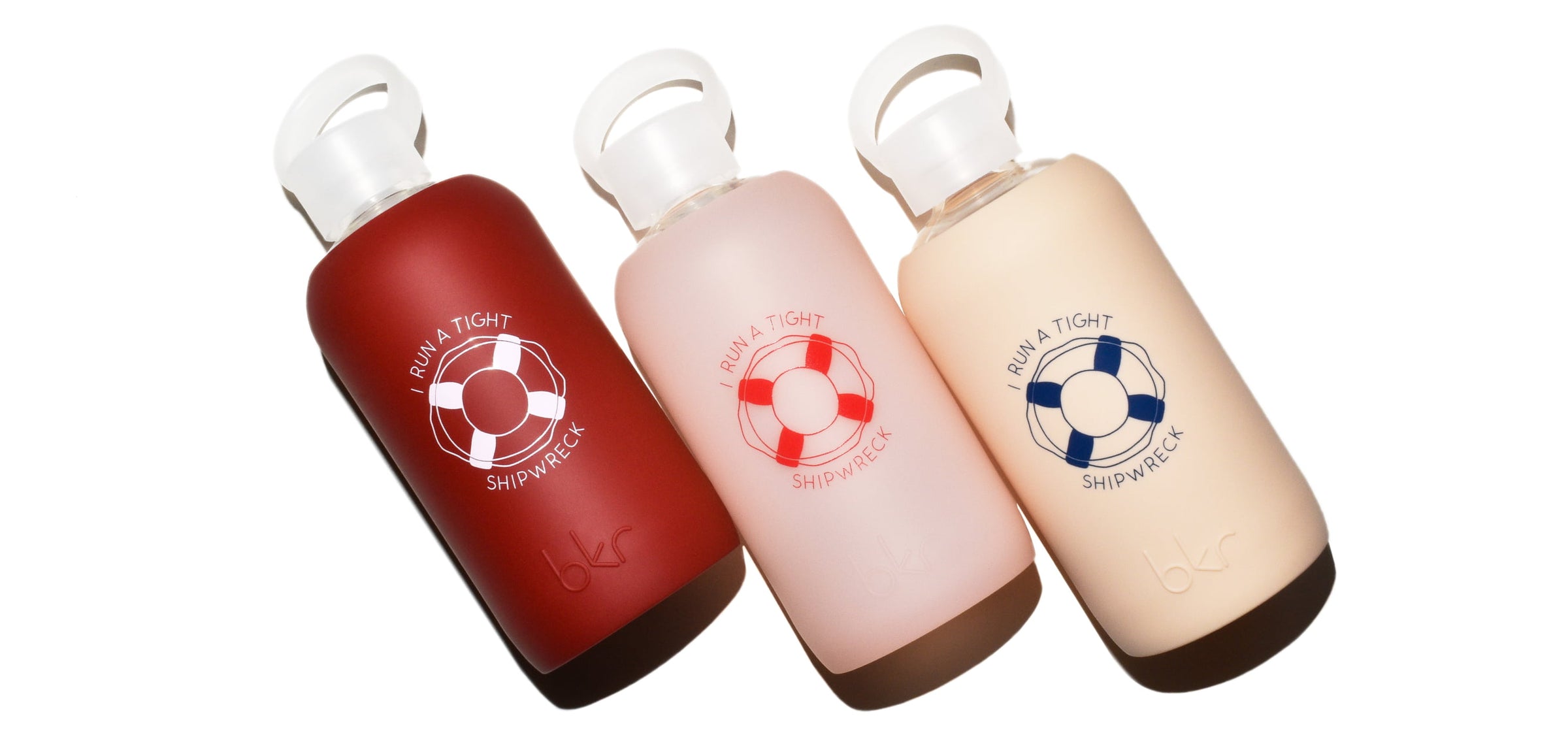 bkr glass and silicone reusable water bottles in opaque Venice brick red with pink "I run a tight shipwreck" print, sheer whispering peach with red "I run a tight shipwreck" print, and opaque linen with blue "I run a tight shipwreck" print.