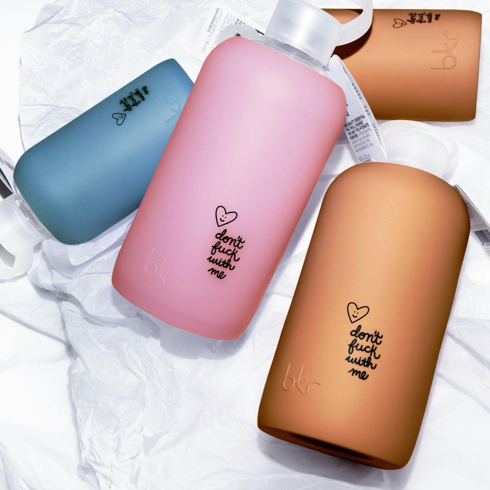Reusable glass and silicone water bottles with black don't fuck with me print in sheer atlantic blue, sheer sugary warm pink, and opaque salted caramel.