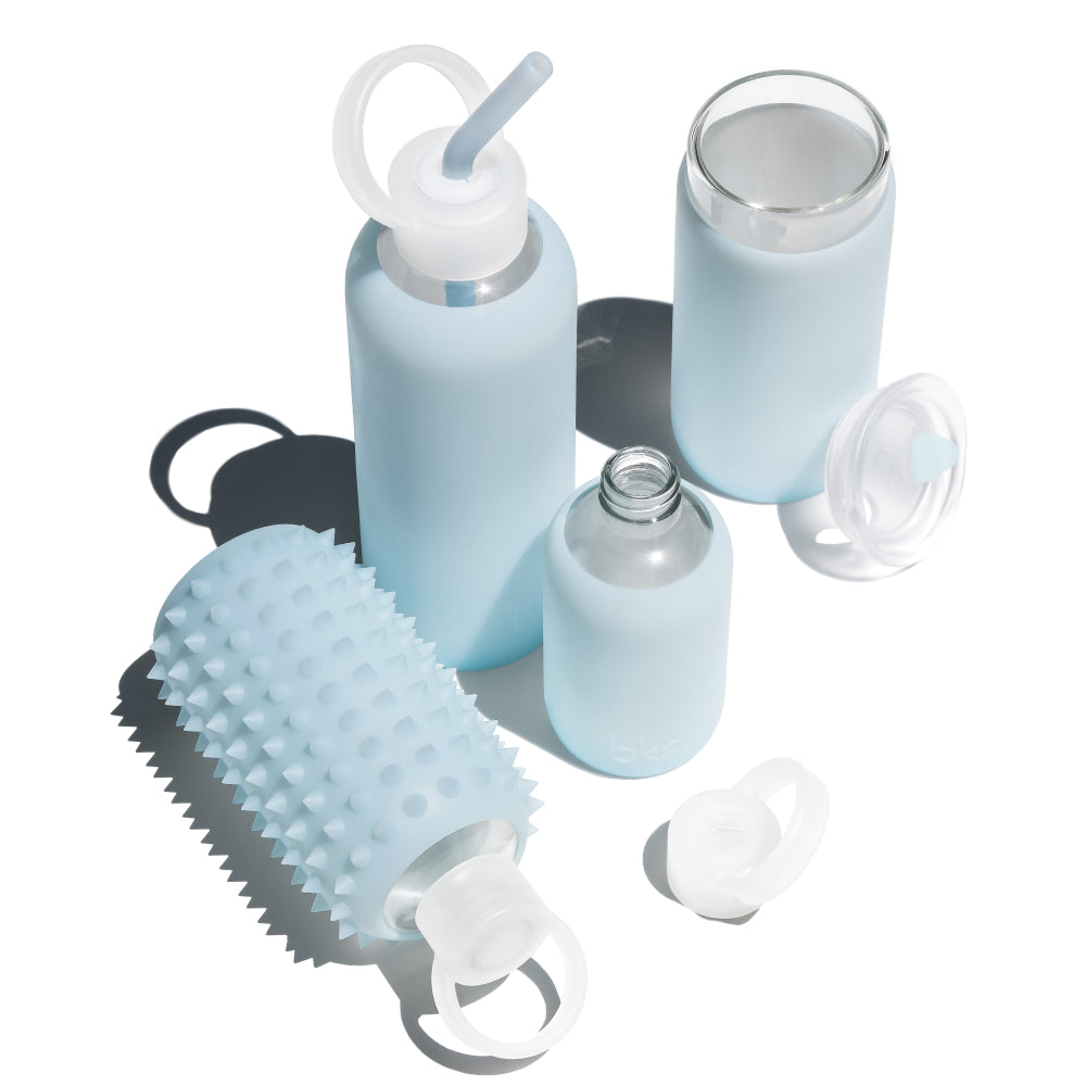 Reusable glass and silicone water bottles in sheer glacial milk blue.