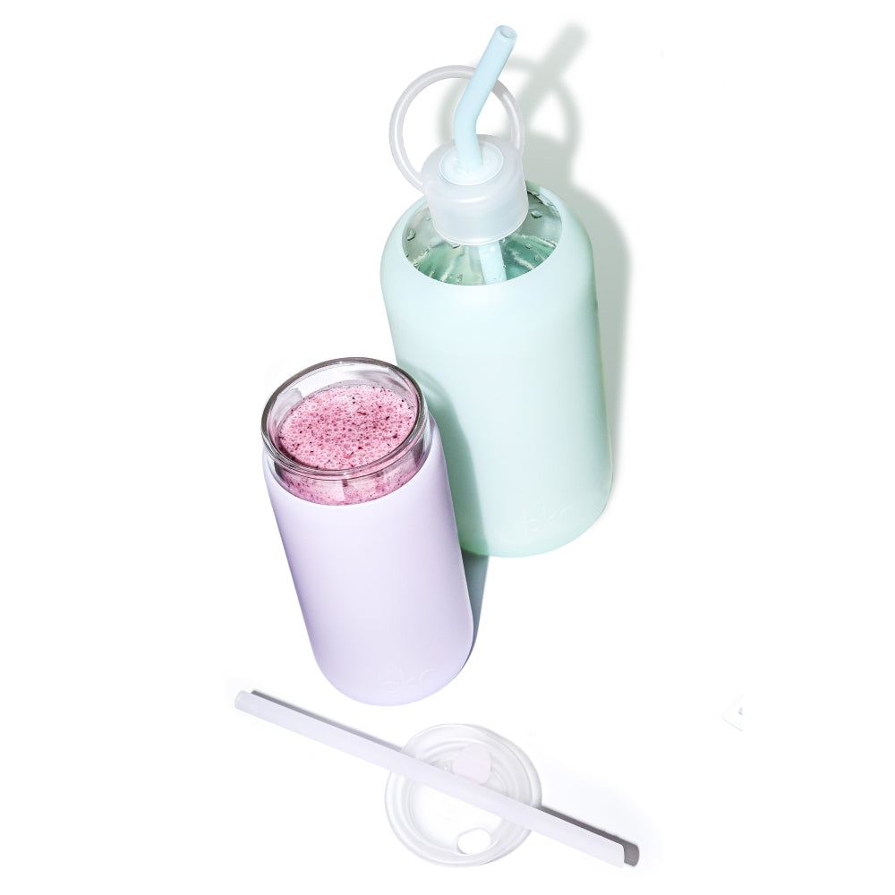 Reusable glass and silicone water bottle and insulated cup in opaque soft sage green and sheer misty lilac.