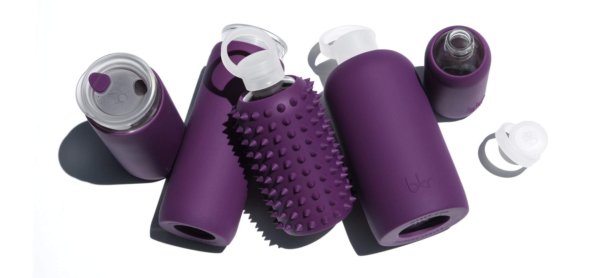 Reusable glass and silicone water bottles in opaque blackcurrant purple.