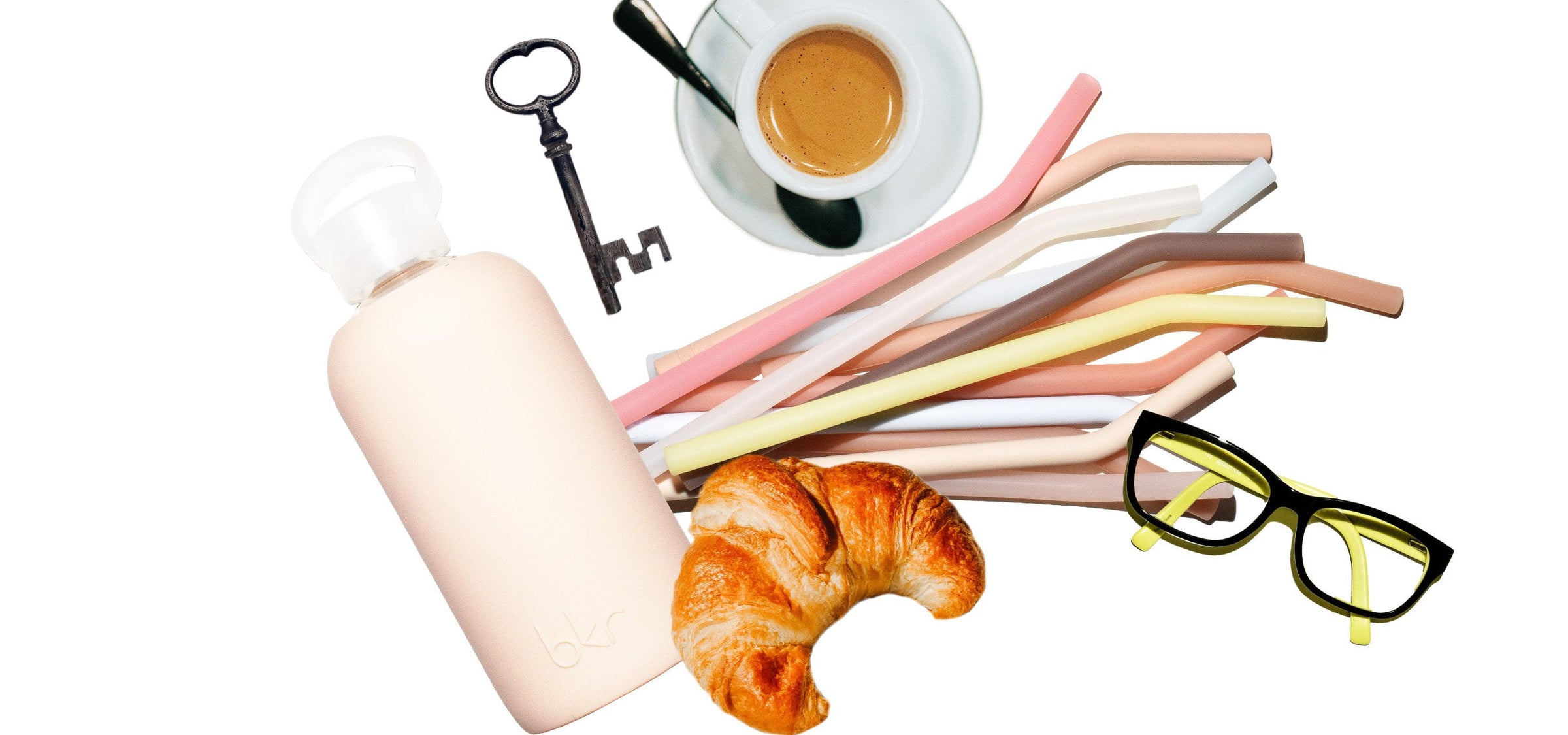 bkr glass and silicone water bottle with assorted straws with an assortment of desk items