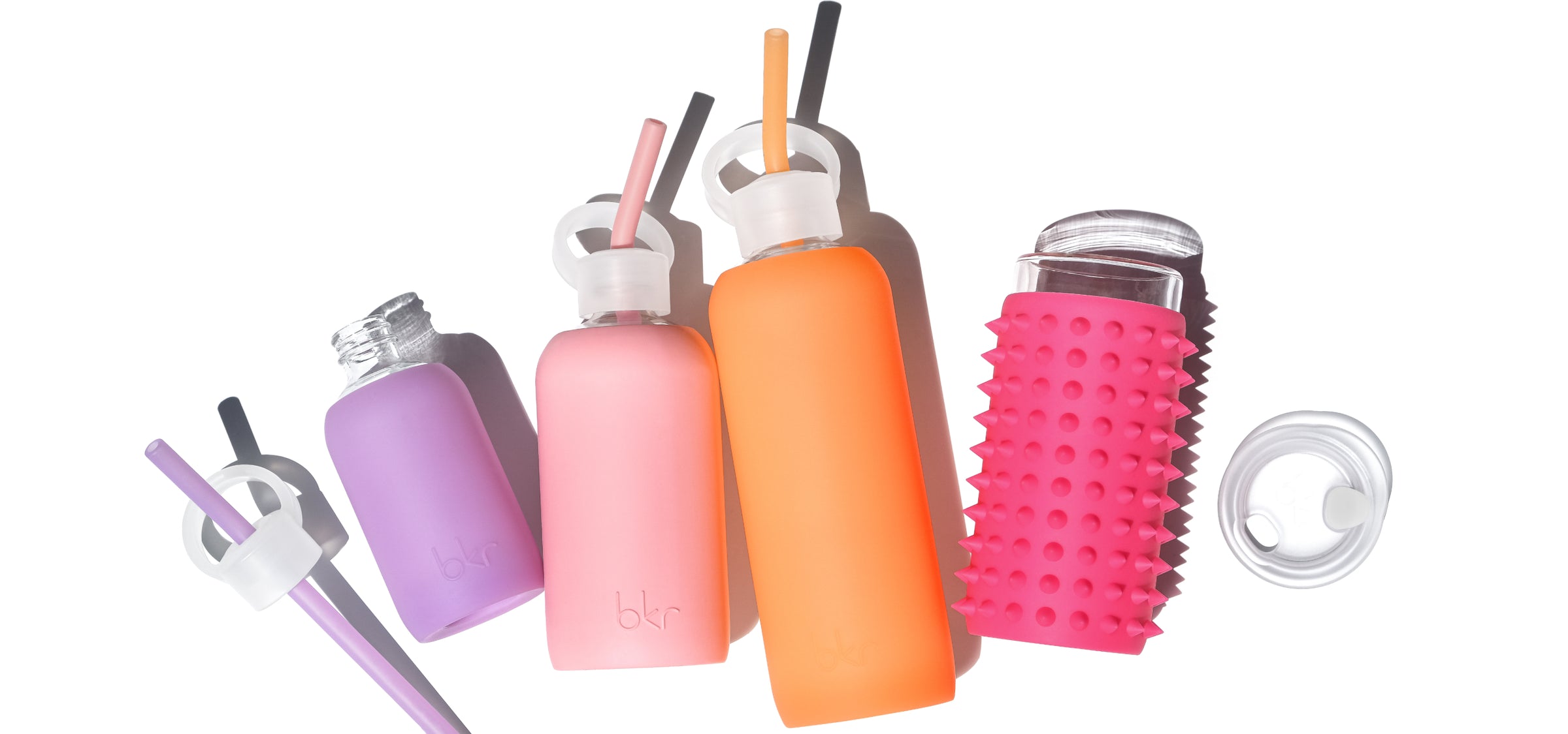 Reusable glass and silicone water bottles in sheer orange cream soda, opaque pastel fluorescent coral, and sheer orchid violet.